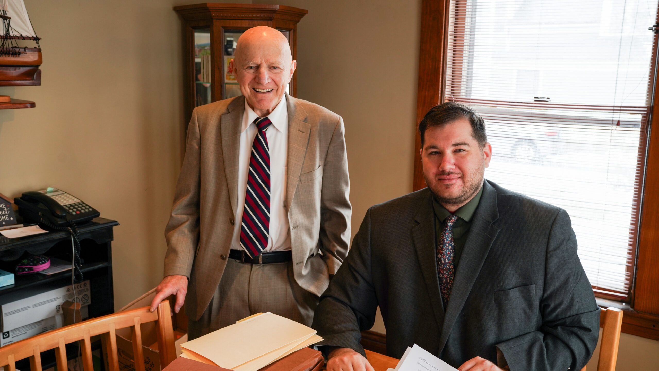 A group of four professionals, two men and two women, are gathered around a conference table reviewing printed charts and documents.