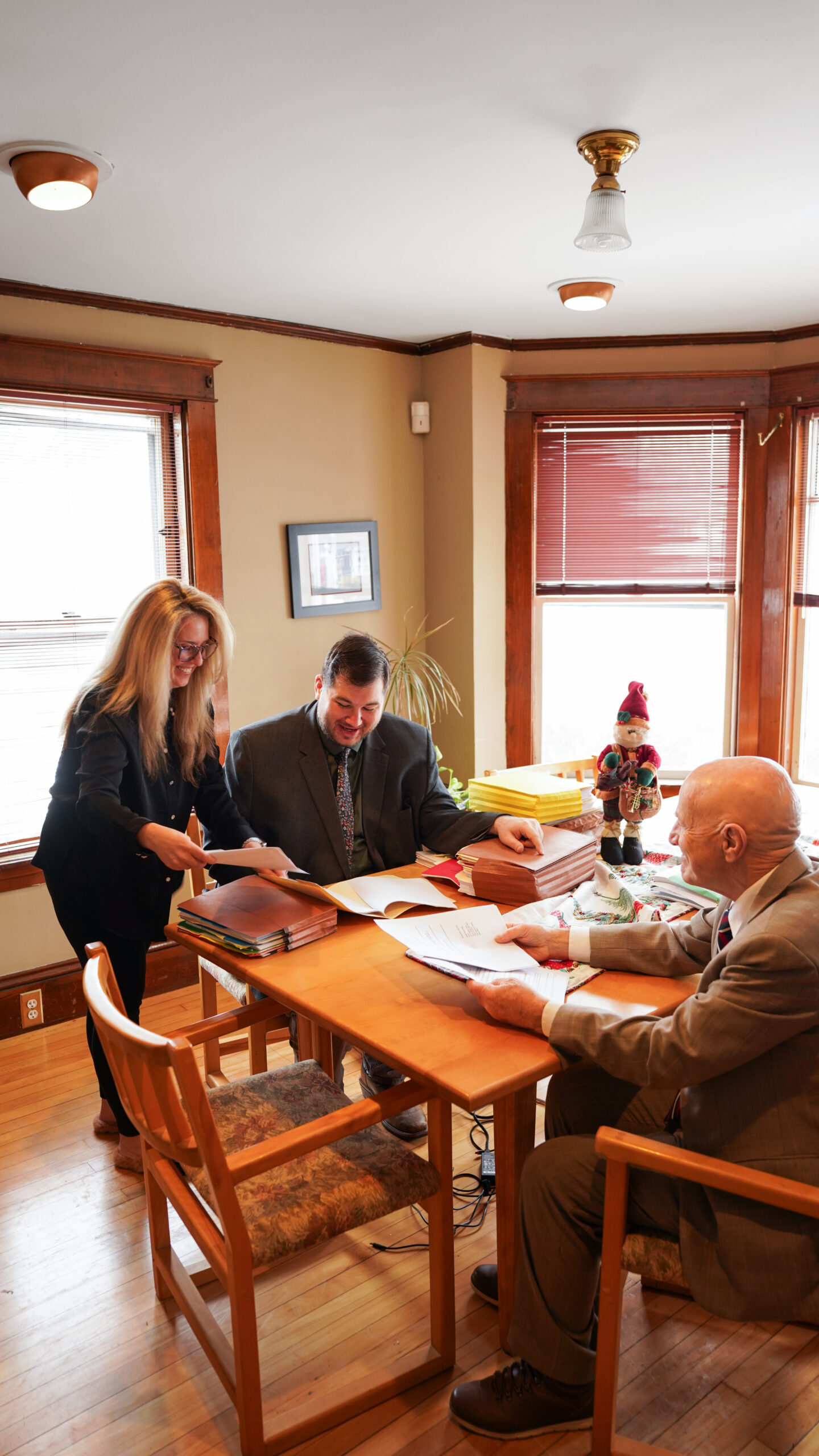 A group of four professionals, two men and two women, are gathered around a conference table reviewing printed charts and documents.
