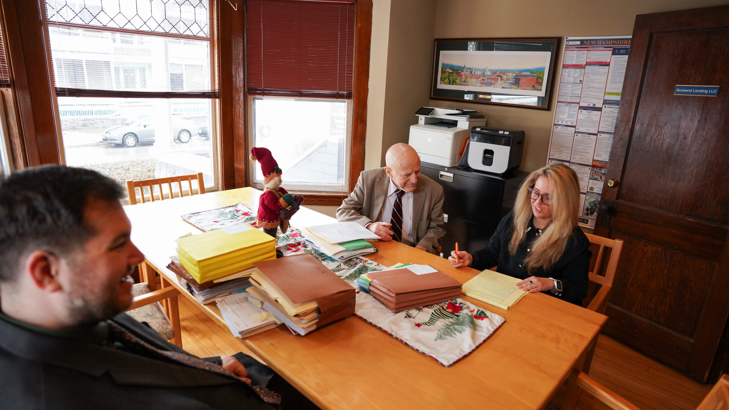 A group of four professionals, two men and two women, are gathered around a conference table reviewing printed charts and documents.