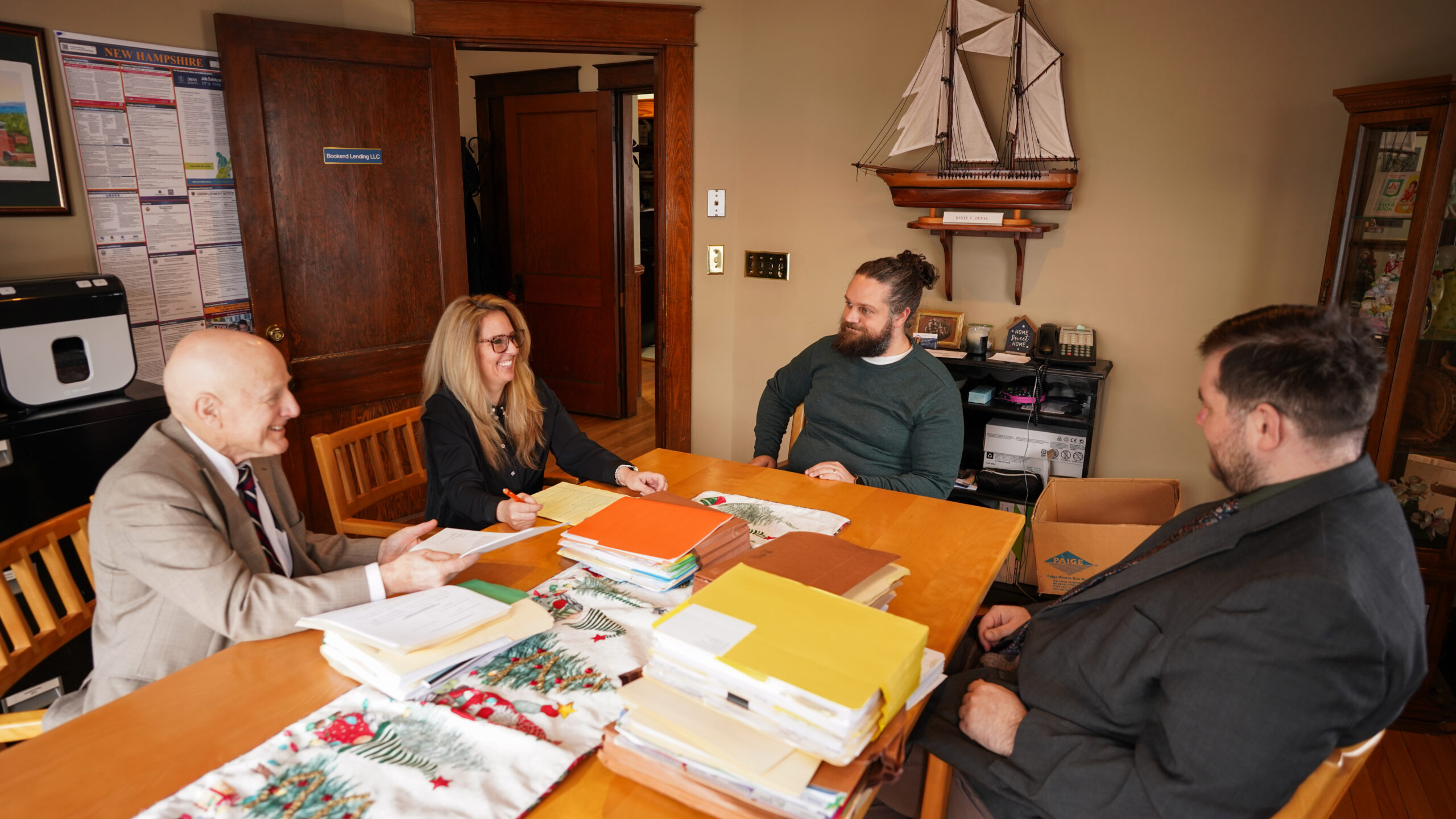 A group of four professionals, two men and two women, are gathered around a conference table reviewing printed charts and documents.